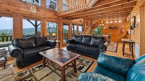 A wooden cabin interior with two leather sofas, a wooden coffee table, and a view through large windows. - Luxury Cabin w/ Games, Views & Hot Tub (Sevierville)