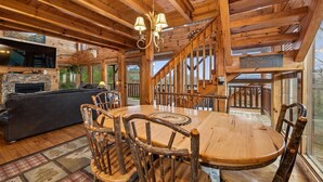 A wooden interior with a fireplace, a round wooden table, rustic chairs, and a staircase. - Luxury Cabin w/ Games, Views & Hot Tub (Sevierville)