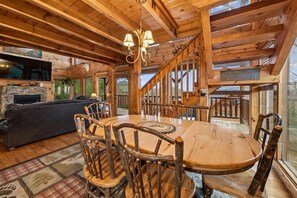 Un intérieur en bois avec une cheminée, une table ronde en bois, des chaises rustiques et un escalier.