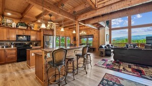 A spacious wooden interior with a kitchen, dining area, and living room, featuring large windows and a view of the outdoors. - Grand Smoky Mountain Cabin w/ Views & Hot Tub (Sevierville)