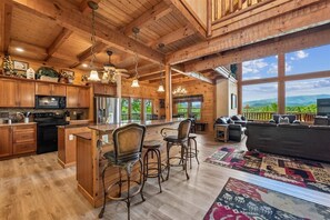 A spacious wooden interior with a kitchen, dining area, and living room, featuring large windows and a view of the outdoors.