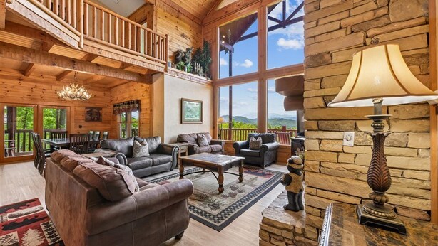 A spacious living room with a wooden ceiling, a balcony, and large windows offering a view of the outdoors. - Grand Smoky Mountain Cabin w/ Views & Hot Tub (Sevierville)