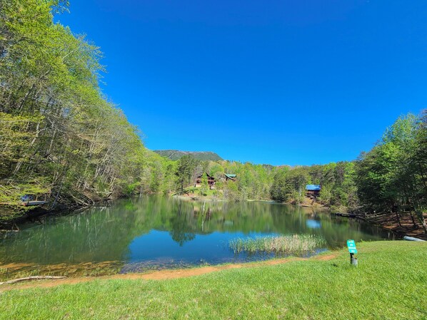 A serene lakeside setting with a small cabin and a grassy area in the foreground.