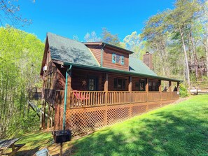 A wooden cabin with a porch, surrounded by a wooden fence and a grassy yard.