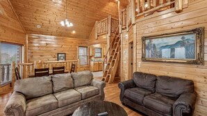 A wooden cabin interior with a dining area, two sofas, a staircase, and a painting on the wall. - Luxe Cabin w/ Breathtaking Smoky Mountain Views (Sevierville)