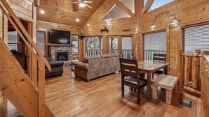 A wooden interior with a fireplace, sofa, dining table, and TV. - Luxe Cabin w/ Breathtaking Smoky Mountain Views (Sevierville)