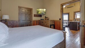 Une chambre avec un grand lit, des murs en bois, un ventilateur de plafond et une vue sur la cuisine.