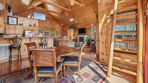 A log cabin interior with a dining area, kitchen, fireplace, and large windows. - Luxury Mountain Cabin w/ Hot Tub & Views (Sevierville)