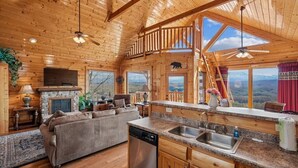 A log cabin interior with a fireplace, kitchen, and a sofa. - Luxury Mountain Cabin w/ Hot Tub & Views (Sevierville)