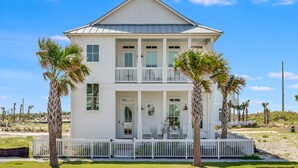 A two-story white building with a balcony, palm trees, and a white fence.
