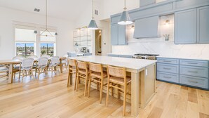 A modern kitchen with a large island, blue cabinets, and wooden chairs.