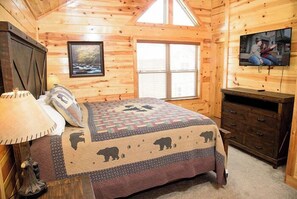 Une chambre confortable dans un chalet en rondins, avec un lit, une commode, un téléviseur et une fenêtre équipée de stores.