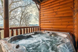 Un bain à remous doté d’une terrasse et d’une rambarde en bois, entouré d’arbres et de montagnes.