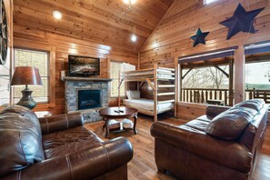 A log cabin interior with leather sofas, a fireplace, a stone wall, and a star decoration on the ceiling.