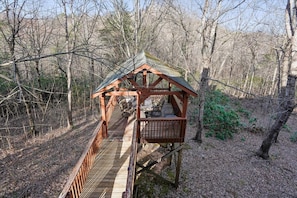 A wooden gazebo with a roof and a platform, surrounded by trees.