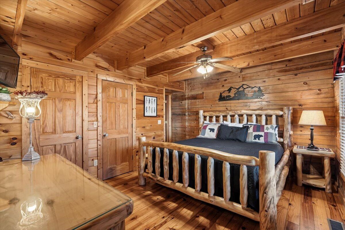 Ein Interieur einer Holzhütte mit einem Bett, einem Deckenventilator und einem Holztisch.