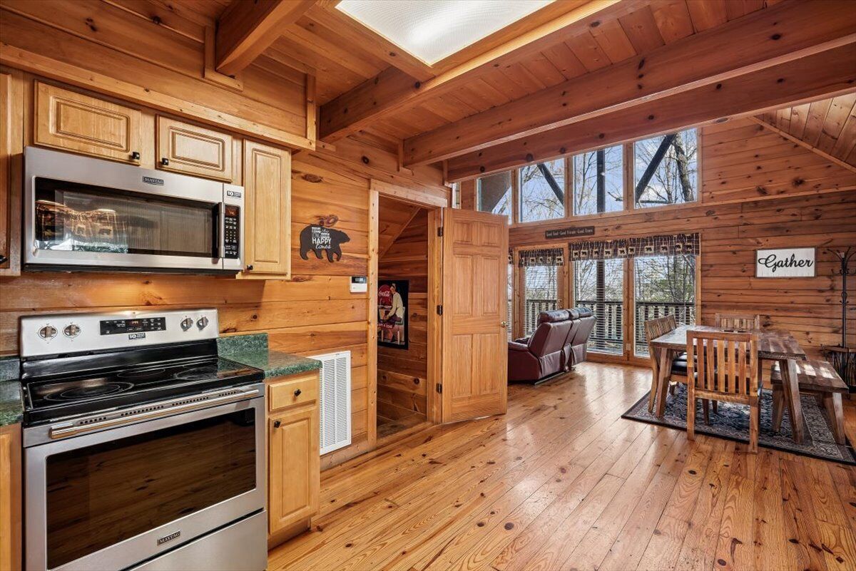 A wooden cabin interior with a kitchen, dining area, and a large window.