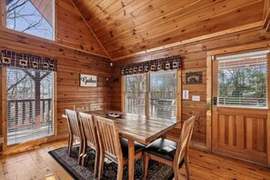A wooden cabin interior with a dining table, chairs, a rug, and a sign that reads 'Cater.'