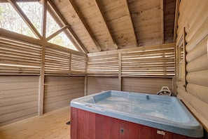 A wooden cabin with a hot tub, wooden floors, and a sloped ceiling.