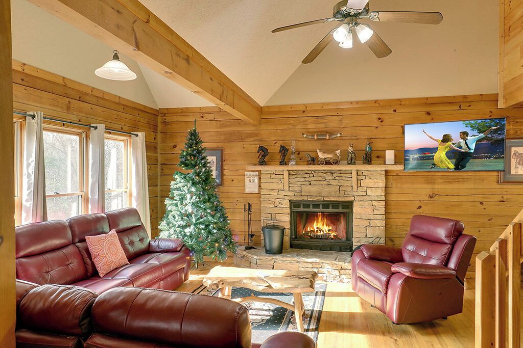 Un interior cálido de cabaña con chimenea, sofás de cuero, un árbol de Navidad y una pared de piedra.