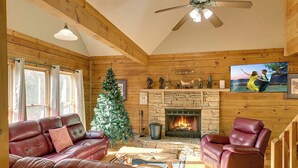 Interior acolhedor de uma cabana com lareira, sofás de couro, árvore de Natal e parede de pedra.