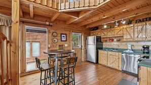 A wooden cabin interior with a dining area, kitchen, and a loft bedroom. - Charming Wooded Cabin w/ Game Area & Views (Sevierville)