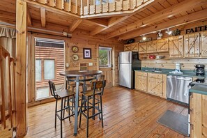 A wooden cabin interior with a dining area, kitchen, and a loft bedroom.