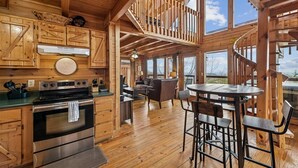 A spacious wooden cabin interior with a kitchen, dining area, and a spiral staircase. - Charming Wooded Cabin w/ Game Area & Views (Sevierville)