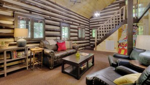 L’intérieur d’une cabane en rondins, avec un escalier, des meubles en cuir et une bibliothèque.