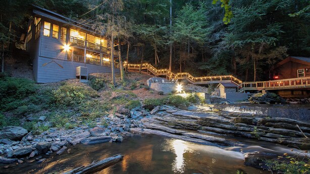 Une cabane dotée d’une terrasse en bois et d’un pont de pierre enjambant un ruisseau.