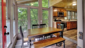 Une cuisine spacieuse avec des meubles en bois, une grande table à manger et une vue sur l’extérieur grâce à de grandes fenêtres.