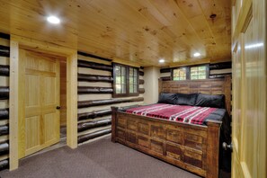 A log cabin bedroom with a wooden bed, a door, and a window. - Enchanting Wooded Cabin w/ Game Room & Hot Tub (Pigeon Forge)