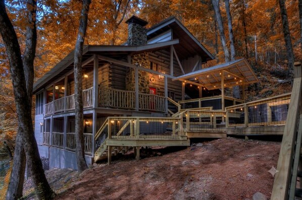 A log cabin with a balcony and a covered outdoor area, surrounded by trees. - Enchanting Wooded Cabin w/ Game Room & Hot Tub (Pigeon Forge)