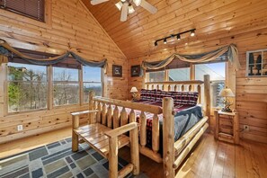 A wooden cabin bedroom with a bed, bench, and large windows.