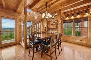 A wooden interior with a dining table and chairs, large windows, and a staircase.
