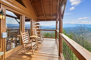 A wooden deck with a view of mountains, a table with chairs, and a lantern.