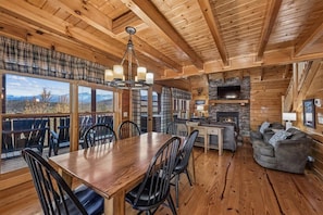 A wooden interior with a dining table, chairs, a fireplace, and a television.