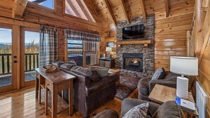 L’intérieur d’une cabane en rondins, avec une cheminée en pierre, des canapés en cuir, un plancher en bois et de grandes fenêtres.