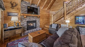 L’intérieur d’une cabane en rondins, avec une cheminée en pierre, un téléviseur fixé au-dessus, un escalier et une pancarte sur laquelle on peut lire « AVENTURE ».