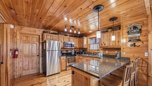 Une cuisine de style rustique, avec des murs en bois, un îlot central, des appareils électroménagers en acier inoxydable et un luminaire suspendu.