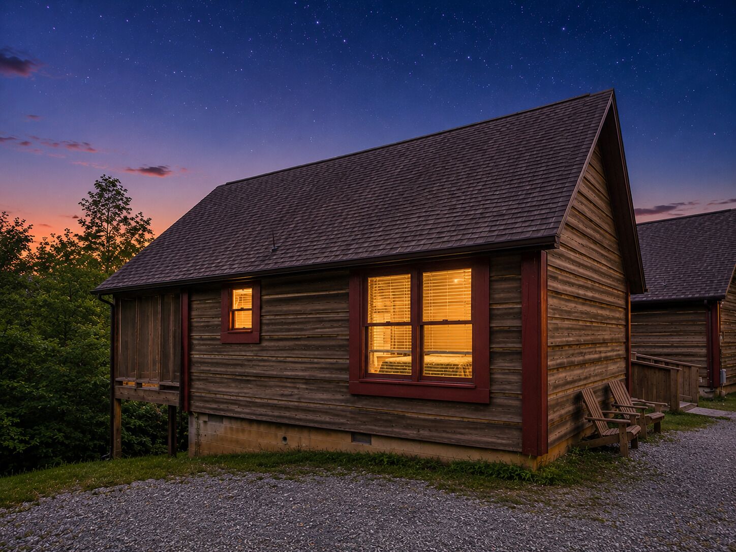 A wooden cabin with a sloped roof, two windows with wooden frames, and a gravel driveway.