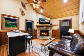 A cozy living area with a stone fireplace, a television mounted above it, and a leather couch.
