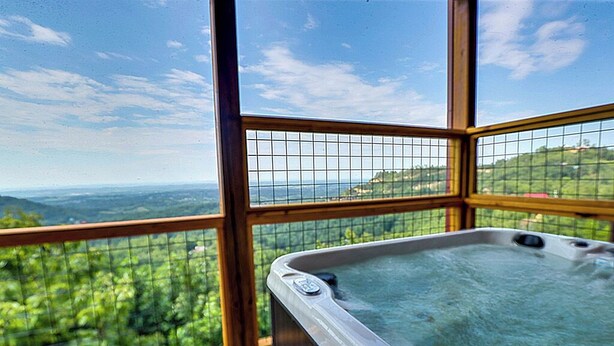 A hot tub with a panoramic view of a lush landscape through large windows.
