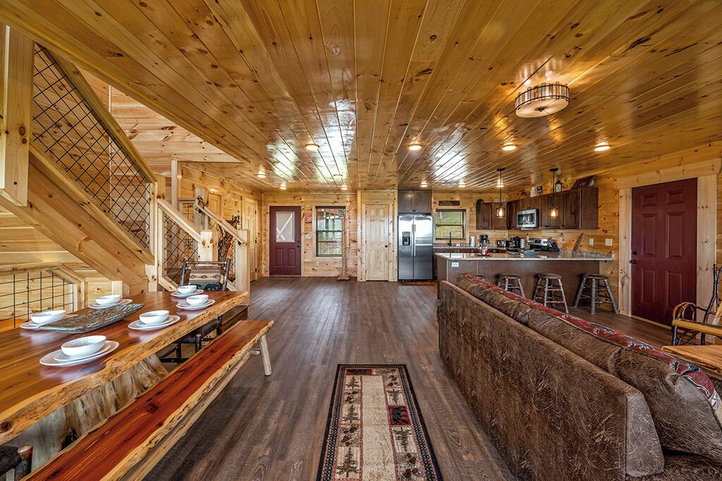 Interior d'una cabana de fusta amb zona de dinar, cuina i escala.