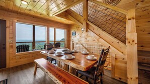A wooden cabin with a dining area, a staircase, and large windows offering a view.