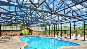 An indoor swimming pool with a glass ceiling, lounge chairs, and a stone wall.