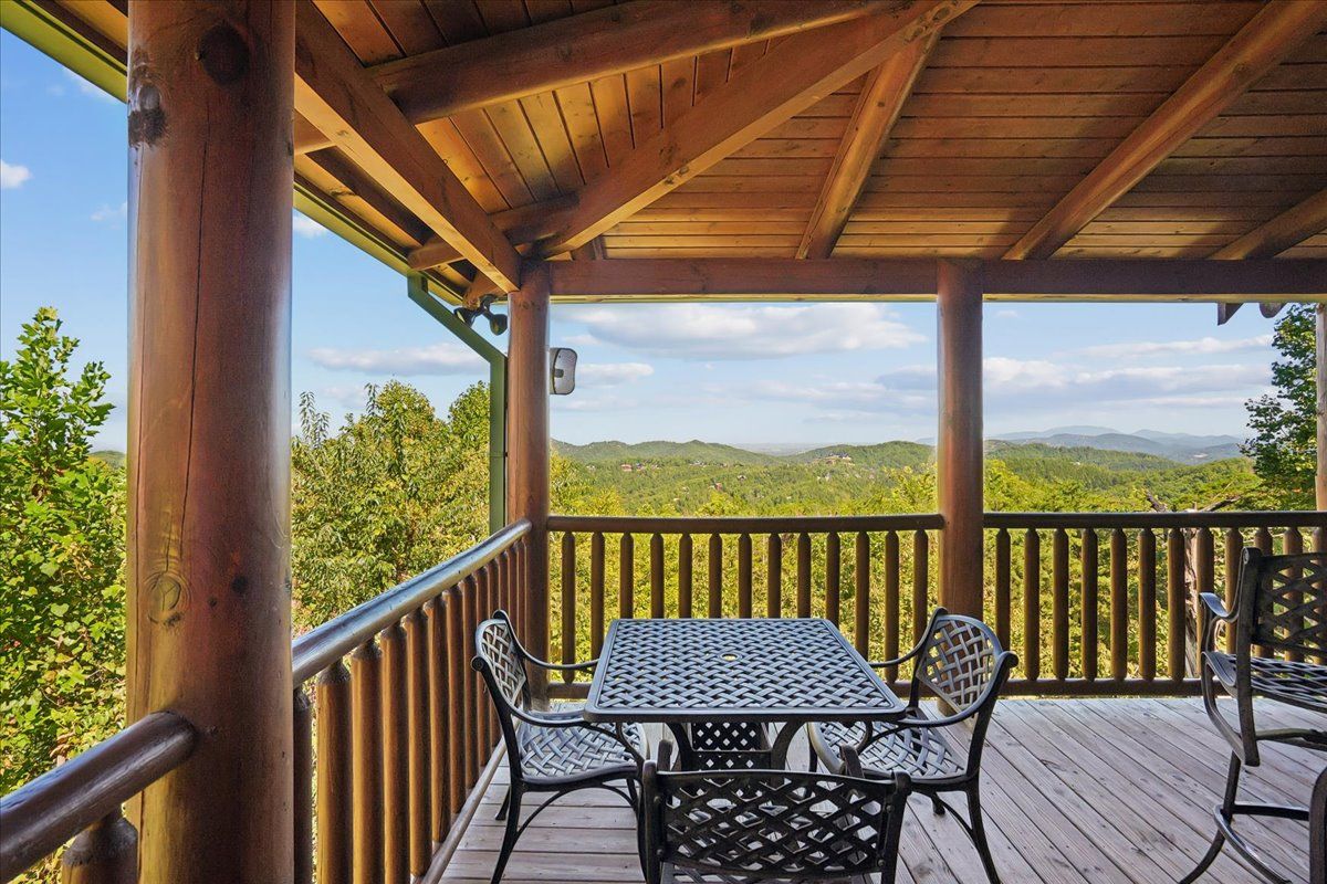 A covered outdoor area with a table and chairs, overlooking a mountainous landscape.