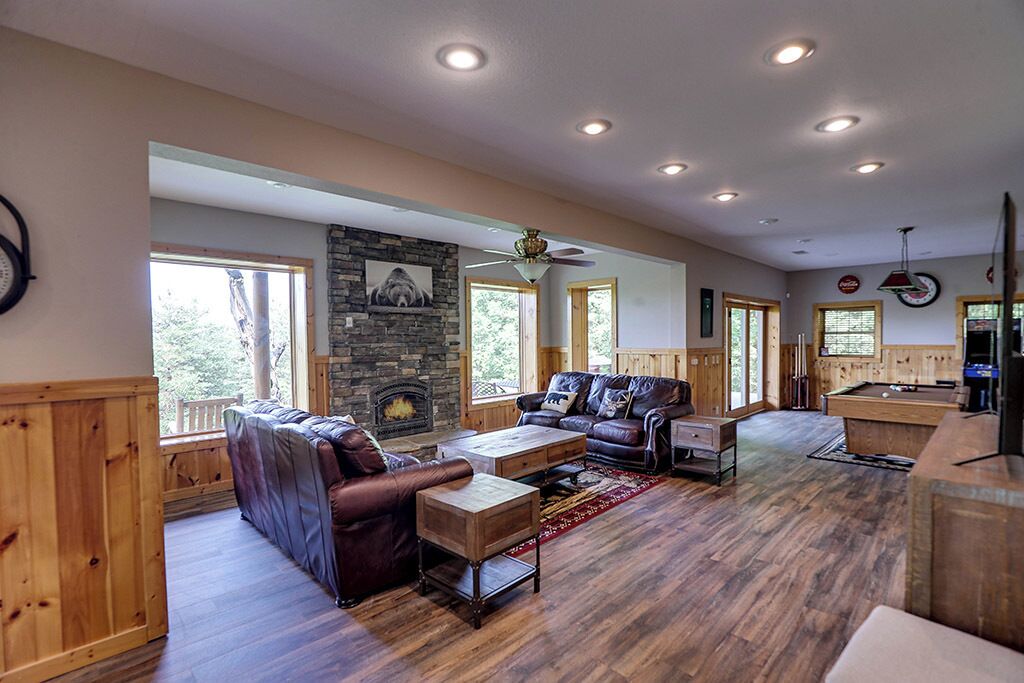 A spacious living room with a fireplace, wooden furniture, and large windows.