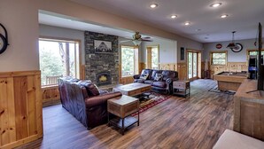A spacious living room with a fireplace, wooden furniture, and large windows. - Spacious Log Home w/ Game Room & Hot Tub (Sevierville)