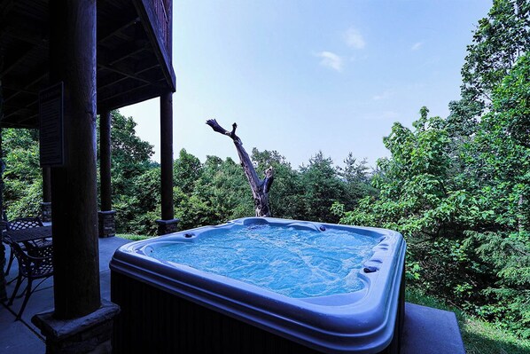A hot tub in a wooded area with a wooden deck and chairs. - Spacious Log Home w/ Game Room & Hot Tub (Sevierville)
